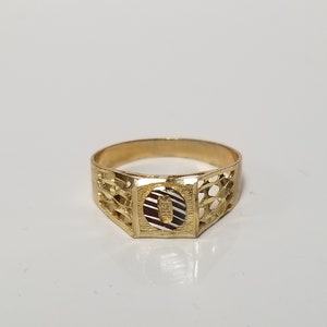 May include: A gold ring with a detailed design and a letter "O" in the centre.