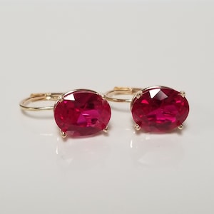May include: A pair of gold hoop earrings with oval-shaped red gemstones. The earrings have a simple design and are perfect for everyday wear.