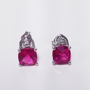 May include: A pair of silver earrings with a square-shaped red gemstone and a small diamond accent.