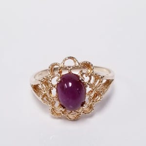 May include: A gold ring with a filigree design and a large oval-shaped ruby gemstone.