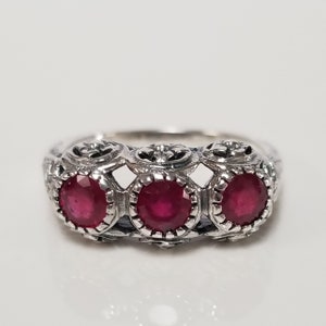 May include: A silver ring with three red ruby stones set in ornate filigree designs.