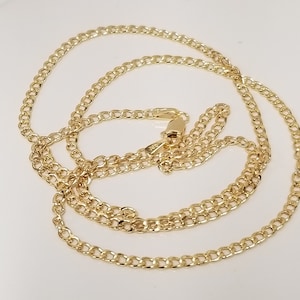 May include: A gold-colored curb chain necklace. The chain is made of small, interlocking links and features a lobster clasp closure. The necklace is displayed on a white surface.