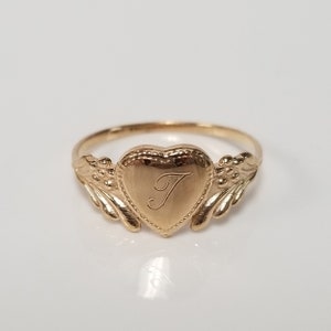 May include: A gold heart-shaped ring with a delicate design and the letter "J" engraved on the front.