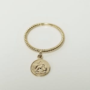 May include: A gold ring with a twisted band and a charm of an angel with wings. The charm is attached to the ring with a small loop.