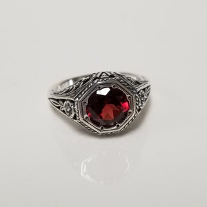 May include: A silver ring with an octagonal, deep red gemstone. The ring has intricate floral and geometric patterns along the band and around the gem. The gemstone is the focal point, set in a detailed, vintage-style setting.