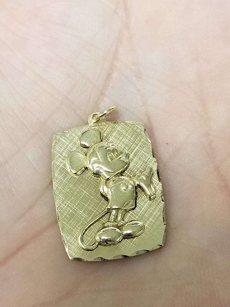 K&ouml;nnte beinhalten: Goldfarbener Anh&auml;nger mit einem erhabenen Bild von Mickey Mouse auf einem rechteckigen, strukturierten Hintergrund. Der Anh&auml;nger hat oben eine kleine Schlaufe f&uuml;r eine Kette. Das Design ist ein klassischer Zeichentrickcharakter.