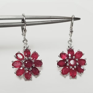 May include: A pair of silver dangle earrings with a red ruby flower design. Each earring features a cluster of oval-shaped rubies set in silver.
