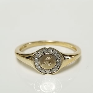 May include: A gold signet ring with a round bezel set with small diamonds and an engraved letter "M" in the center.
