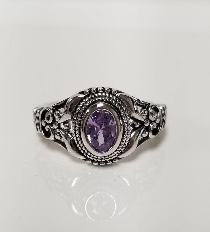 May include: A silver ring with an ornate design and a purple oval gemstone.