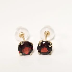 May include: A pair of gold stud earrings with oval, deep red gemstones. The earrings have a classic design with a post and backing for secure wear. The gemstones are set in a gold bezel setting.