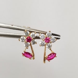 May include: A pair of gold earrings with a flower design. The flowers are made of white and pink cubic zirconia stones. The earrings have a dangling pink cubic zirconia stone.