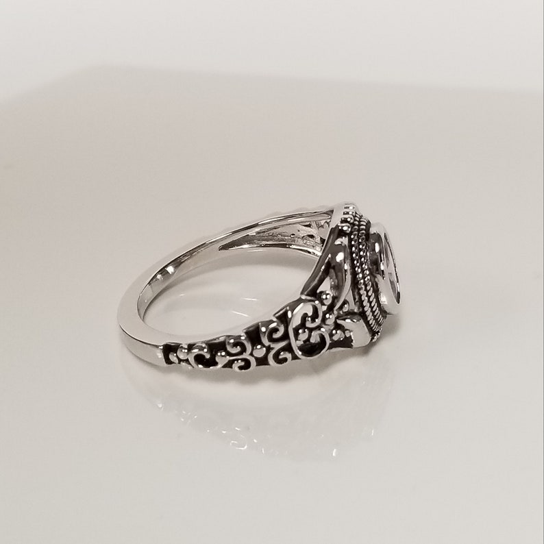 May include: A silver ring with an ornate design. The ring has a filigree pattern and a round stone in the center.