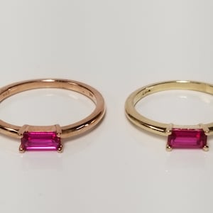 May include: Two simple gold rings with a single pink rectangular gemstone set in the centre of each ring. The ring on the left is rose gold and the ring on the right is yellow gold.