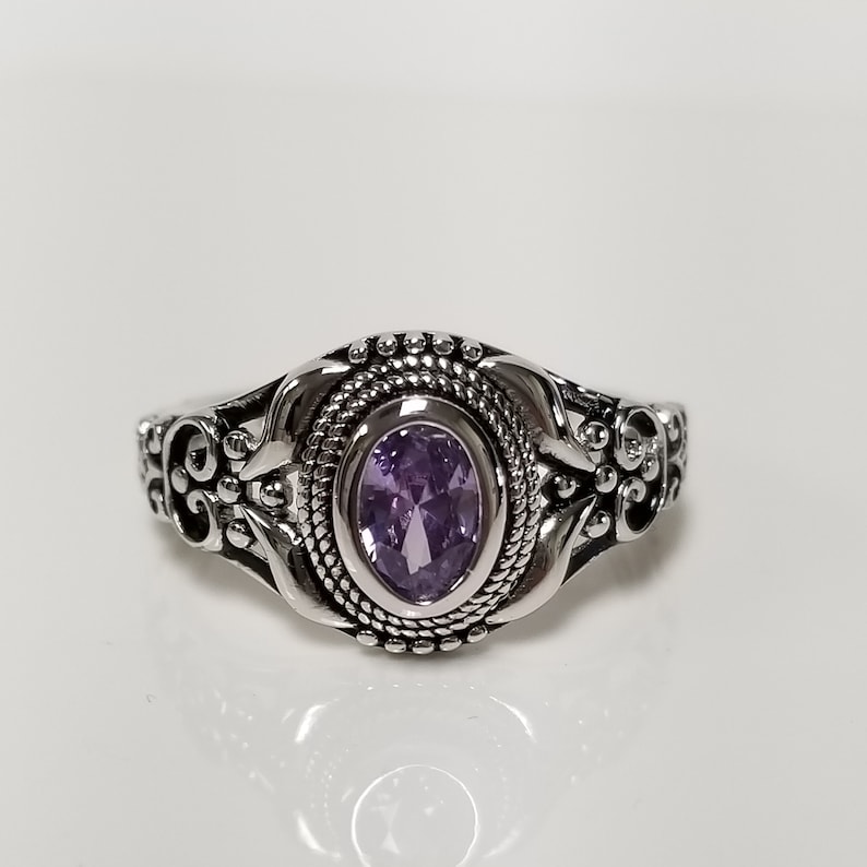 May include: A silver ring with an ornate design and a purple oval gemstone.