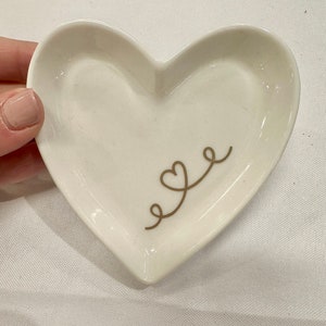 May include: White heart-shaped ceramic dish with a gold design of two intertwined hearts.
