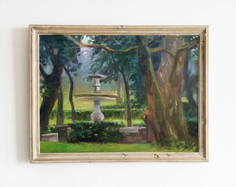 Op de afbeelding: Een ingelijst olieverfschilderij dat een fontein in een tuinomgeving toont. De fontein is wit en heeft een rond bassin. De tuin is weelderig en groen met bomen en struiken. Het schilderij is ingelijst in een licht houten lijst.