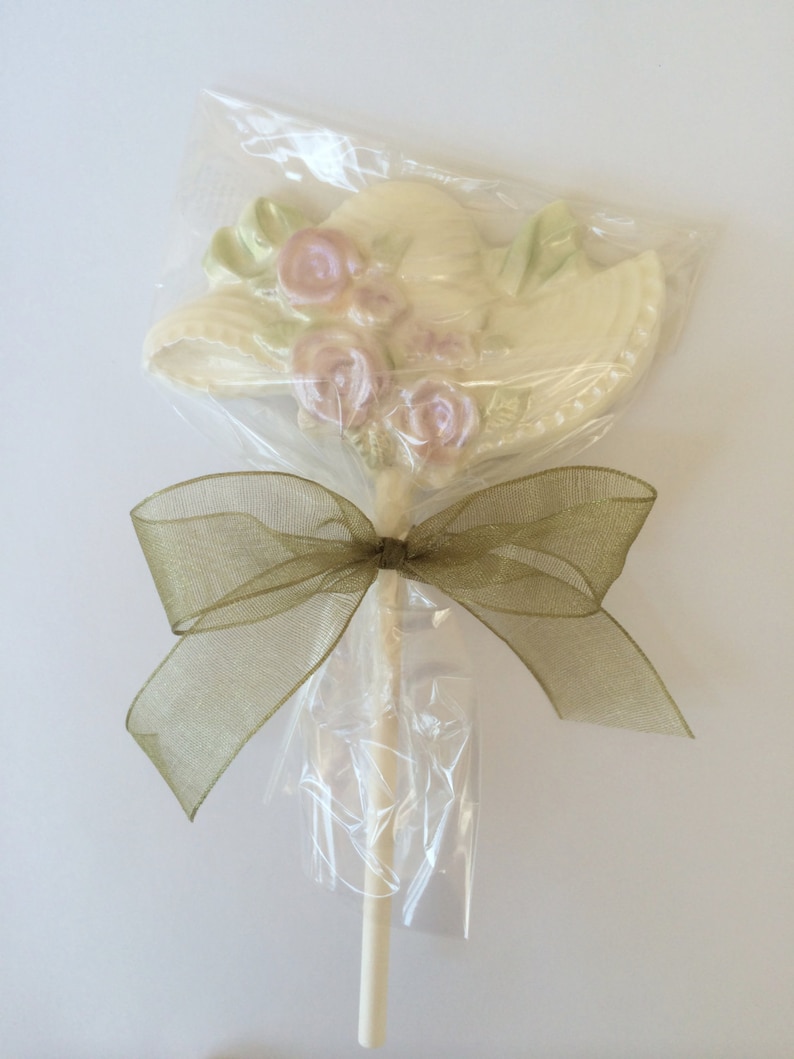May include: A white chocolate hat with pink flowers on a stick, wrapped in clear cellophane and tied with a brown ribbon.