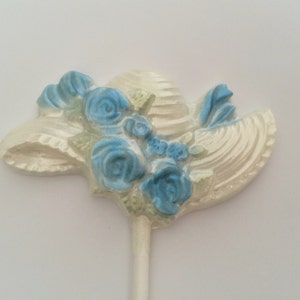 May include: White chocolate hat with blue flowers on a stick. The hat is decorated with a white ribbon.