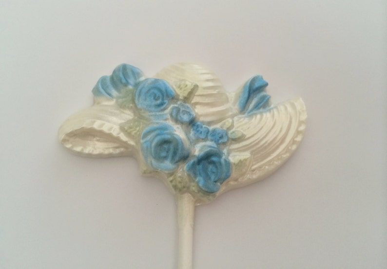 May include: White chocolate hat with blue flowers on a stick. The hat is decorated with a white ribbon.
