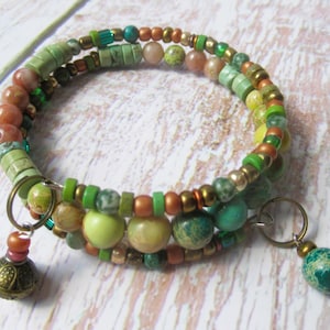 May include: A multi-strand wrap bracelet with a mix of green, brown, and gold beads. The bracelet includes various sizes and shapes of beads, with a few decorative charms. The colour palette is earthy, with shades of green, brown, and gold.