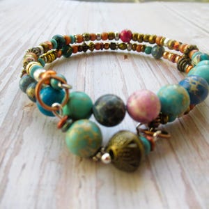 May include: A multi-strand bracelet featuring turquoise, pink and brown beads. The bracelet is crafted from a mix of materials, including metal and glass beads.