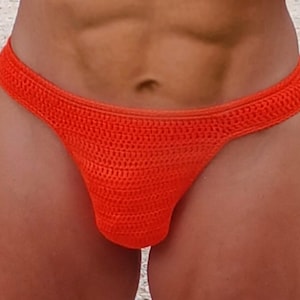 May include: A vibrant orange crochet bikini bottom. The handmade swimwear has a low-rise design with a textured, open weave. The bright colour and unique construction make it a standout piece for beach or poolside wear.