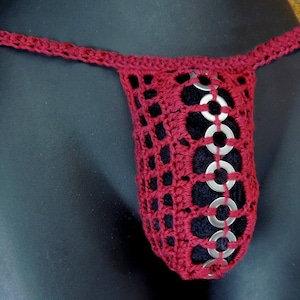 May include: A red crocheted garment with silver metal rings. The garment is made of a delicate, open-weave fabric.