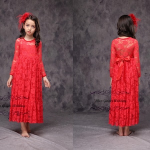 May include: A red lace dress with long sleeves and a bow at the waist. The dress is floor-length and has a fitted bodice. The model is wearing a red flower headband.