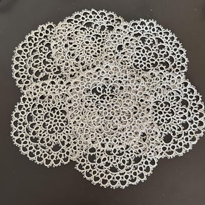Pode incluir: Uma coleção de toalhinhas de renda circulares em tom branco sujo, apresentando um intrincado trabalho de frivolité com delicados padrões florais repetitivos e bordas festonadas, dispostas em um grupo sobreposto para exibir o fino trabalho.