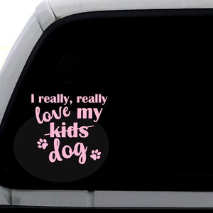 May include: A black and white car window decal with pink text that reads "I really, really love my kids dog" with paw prints around the word "dog".