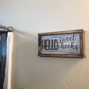 Puede incluir: Un letrero de madera con fondo blanco y letras marrones. El letrero dice "HELLO sweet cheeks".