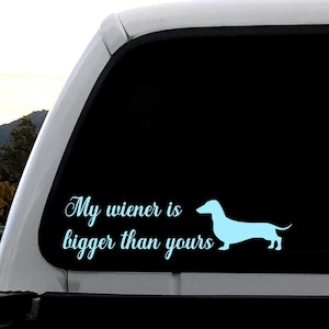 May include: A white truck with a black window decal that says "My wiener is bigger than yours" and a light blue silhouette of a dachshund.