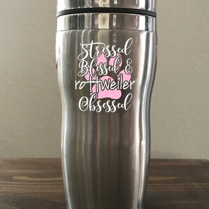May include: Stainless steel travel mug with a white design that says "Stressed Blessed & Rottweiler Obsessed" with a pink paw print.