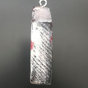 Pu&ograve; includere: Un ornamento in legno bianco e nero con un design rosso e bianco. L'ornamento ha un anello d'argento in cima per appenderlo.