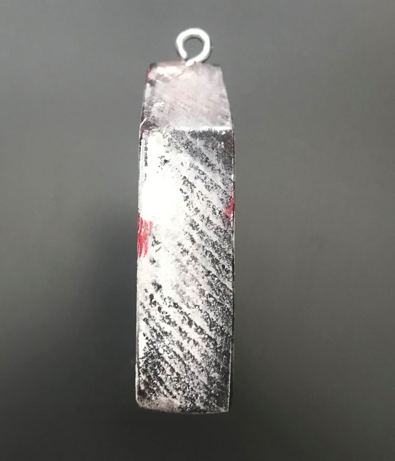 Pu&ograve; includere: Un ornamento in legno bianco e nero con un design rosso e bianco. L'ornamento ha un anello d'argento in cima per appenderlo.