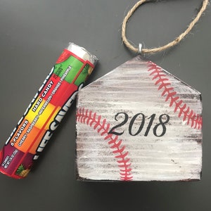 Pu&ograve; includere: Un ornamento per la casa in legno bianco a forma di piatto di casa da baseball con cuciture rosse e l'anno 2018 dipinto su di esso. L'ornamento ha un gancio in corda.
