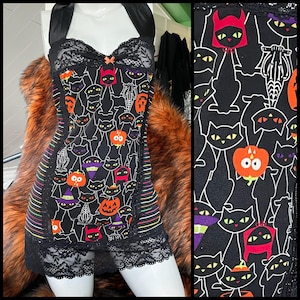 May include: Black lingerie set with a Halloween-themed cat print. The top features a halter neck, lace trim, and a small bow. The shorts have a matching print and lace trim. The print includes black cats, pumpkins, and witch hats.