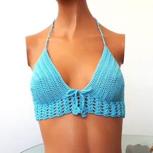 May include: A turquoise crochet halter top with a V-neck design. The top features a tie closure at the bust and a scalloped edge along the bottom. The crochet work is visible, showcasing the texture and pattern of the garment.