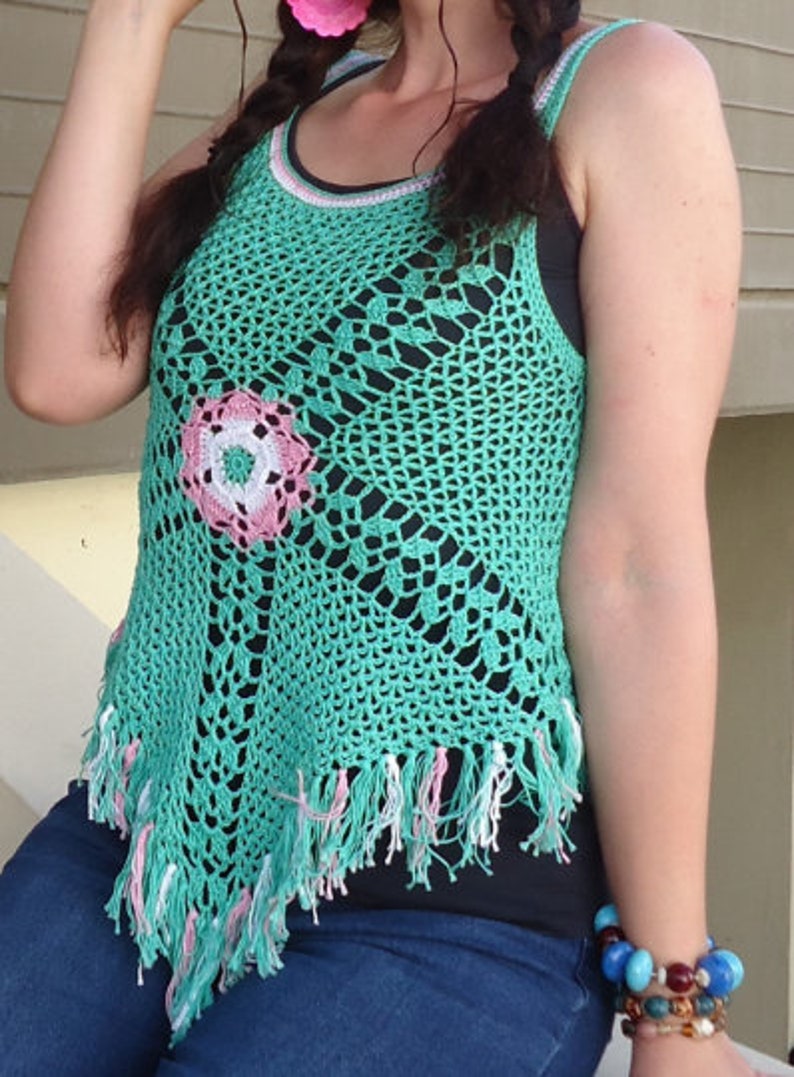 May include: A green crochet top with a pink and white flower design. The top has a fringed hem and is sleeveless.