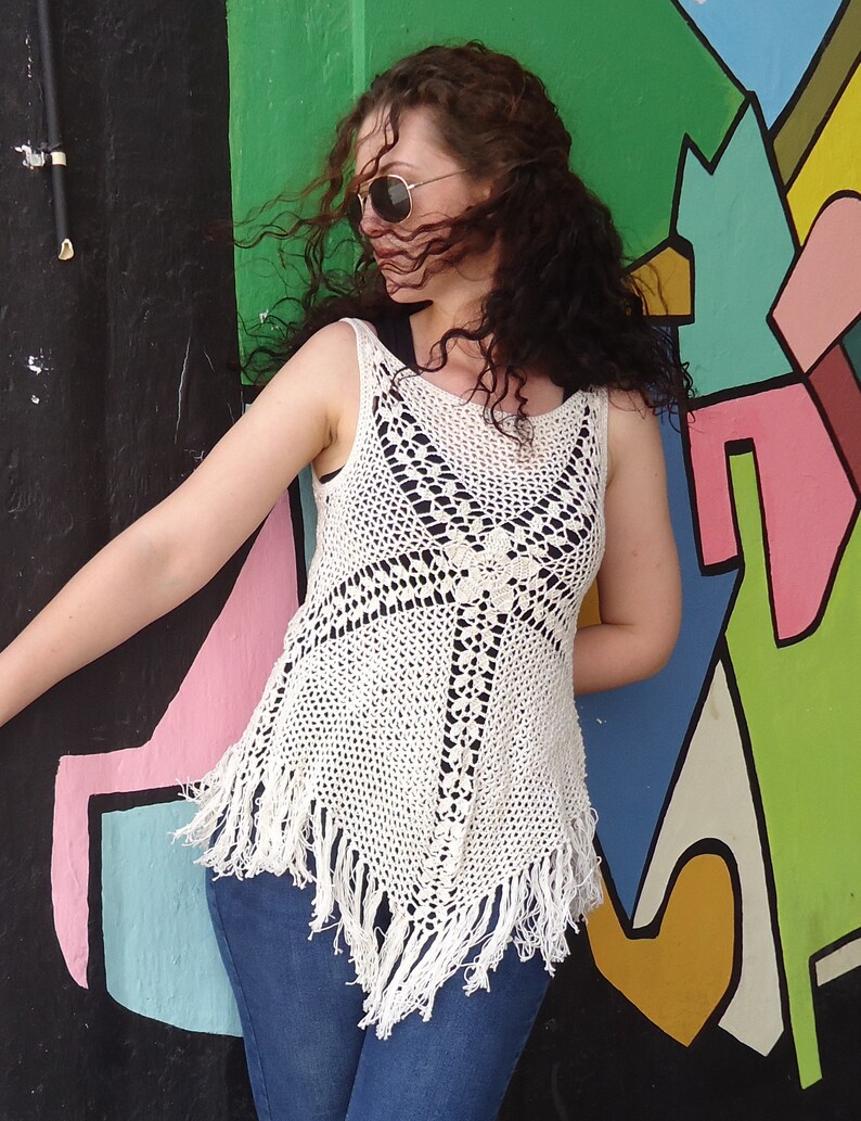 May include: A white crocheted top with fringe detailing. The top has a geometric pattern and is worn over blue jeans.