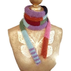 May include: A long, fuzzy knit scarf featuring a vibrant color-blocked pattern with stripes of lavender, deep red, olive green, light blue, pink, and orange. The scarf is wrapped around the neck of a gold-toned mannequin torso with a butterfly graphic.