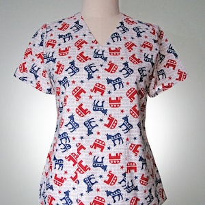 Op de afbeelding: Een wit scrubshirt met een patroon van rode olifanten en blauwe ezels, met de woorden "Democrat" en "Republican" die steeds worden herhaald.