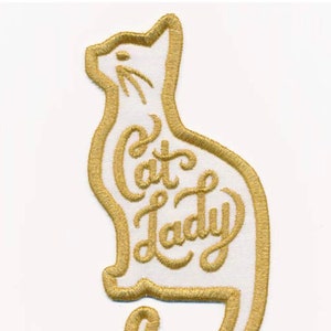 May include: Gold embroidered iron-on patch shaped like a cat with the text "Cat Lady" inside the outline.