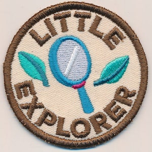 May include: Brown embroidered patch with the words "Little Explorers" in a circle around a blue magnifying glass with a pink handle and two green leaves.
