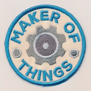 May include: A blue and white embroidered patch with the text "Maker of Things" and a silver gear in the centre.