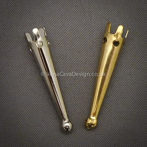 Könnte beinhalten: Zwei Häkelnadeln aus Metall, eine silberne und eine goldene, mit einer spitzen Spitze und einem dekorativen Oberteil.