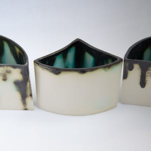 May include: Three ceramic planters in a triangular shape with a white glaze and black accents. The planters have a drip glaze effect on the rim.