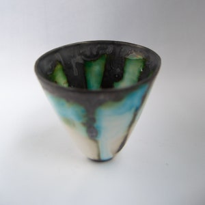 May include: A handmade ceramic bowl with a unique, asymmetrical shape. The rim is dark gray, transitioning to shades of green, blue, and white. The bowl's interior features a glossy finish, creating a striking contrast.
