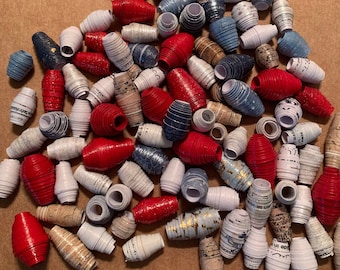 May include: A collection of paper beads in red, white, and blue colors. The beads are made from rolled up paper and have a variety of patterns and textures.