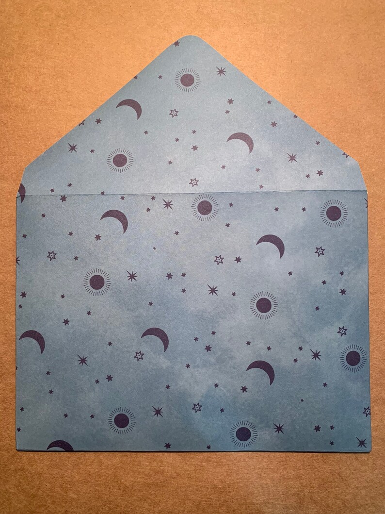 May include: A blue envelope with a pattern of stars, moons, and suns. The envelope is made of paper and has a textured surface.